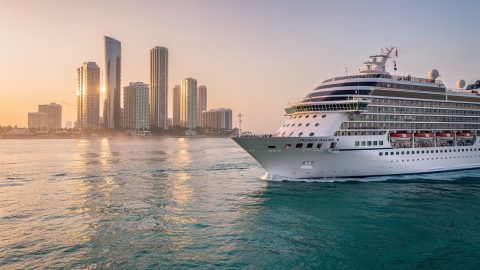 Vue d’un paquebot quittant le port de Miami en direction des Caraïbes, avec la skyline illuminée par le lever du soleil.
