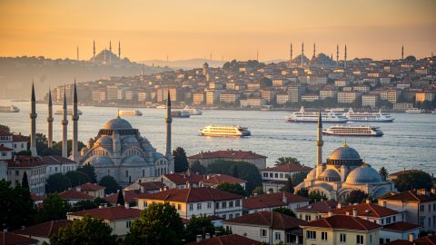 Vue panoramique d’Istanbul au coucher du soleil, avec des ferries naviguant sur le Bosphore, les mosquées et les toits de la vieille ville baignés d’une lumière dorée.