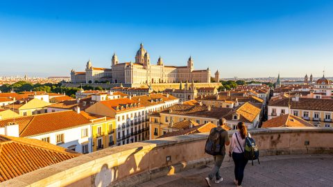 Vue panoramique lumineuse de Madrid depuis les hauteurs, avec le Palais royal, les toits ocre, un ciel bleu et deux voyageurs dans le centre historique.